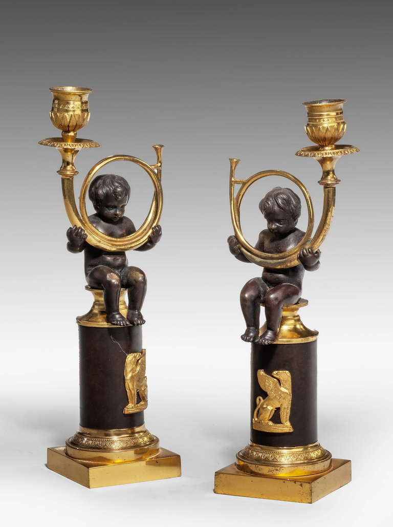 An attractive pair of Regency period bronze and gilt bronze putti candlesticks, the children supporting candlesticks in the form of horns, the circular base mounted with exotic birds in relief.

