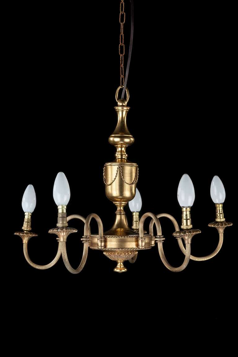 A mid-20th century five-arm brass chandelier with scroll supports over an Adam design central section.