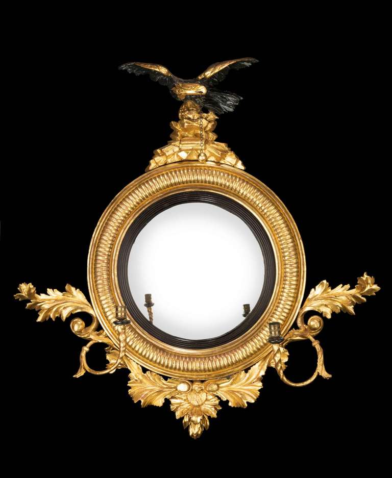 Fine Regency period convex mirror with ebony inner border, the top with rocaello pediment surmounted with an eagle, the lower section with two candleholders.

RR.