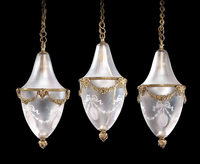 An unusual set of three antique pear shaped lanterns, delicately chiseled swags with flowers and foliage supports with ram's heads, original condition including glazing.