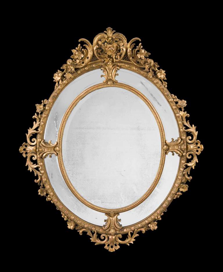 A fine French oval 19th century giltwood mirror, with bevelled border plates and elaborate scrollwork, flowers and foliage, retaining original gilding.