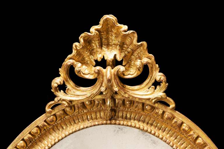 A very fine Chippendale period oval giltwood mirror, the top section with a stylized shell, the border crisply carved.

