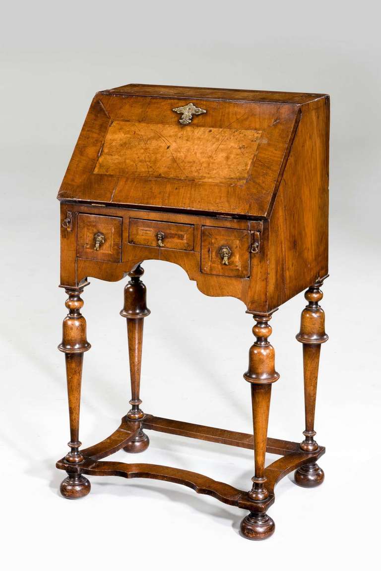 A tiny walnut Bureau of William and Mary design on baluster supports joined with wavy cross stretchers, the broadly crossbanded fall with feather banding, the serpentine fronted interior with doors and pigeon whole flanking a centre door with