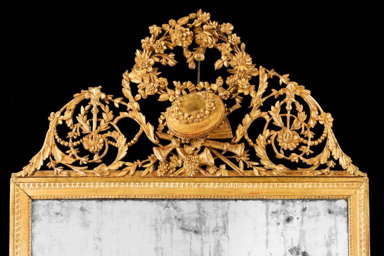 A very finely carved 18th century giltwood mirror, the top elaborately carved with pierced folios and scrolls, the centre section of the mirror with carving signifying the arts and music, below beaded outer edge with replacement 19th century plate.

