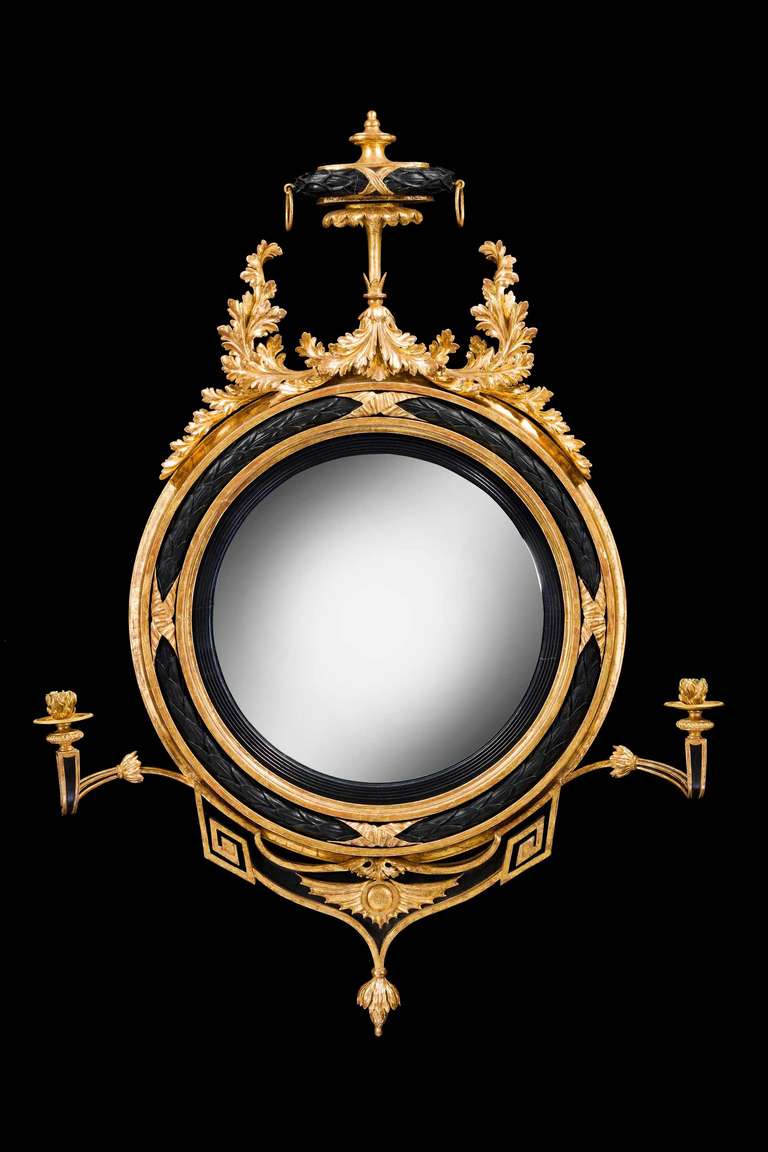 A very fine Regency period convex circular mirror, alternate decoration ebonized and giltwood with two finely swept and delicate arms incorporating candelabra, the top section with swept scroll work beautifully carved with oak leaves together with