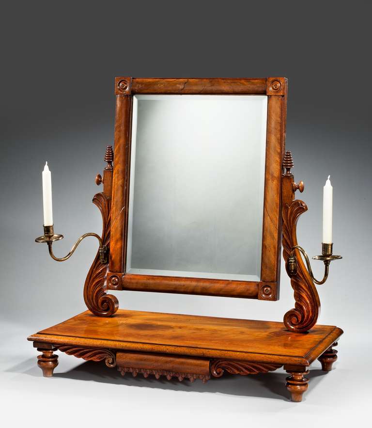 An exceptionally fine Regency period mahogany dressing mirror, the centre section concealing a drawer, the flared uprights supporting two brass candle sticks. Bevel plate.