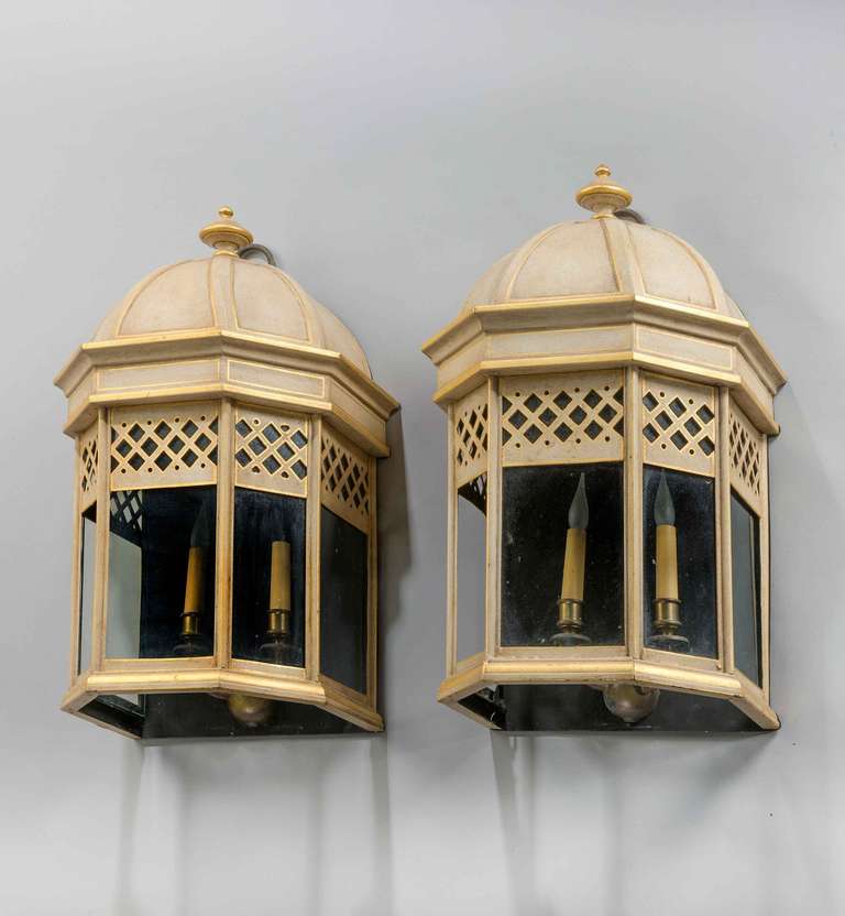 Pair of 20th century Tole wall lanterns, the glass sections under a diamond pierced border with shaped tops. Soft ivory decorated enamel with muted gilding.

RR.