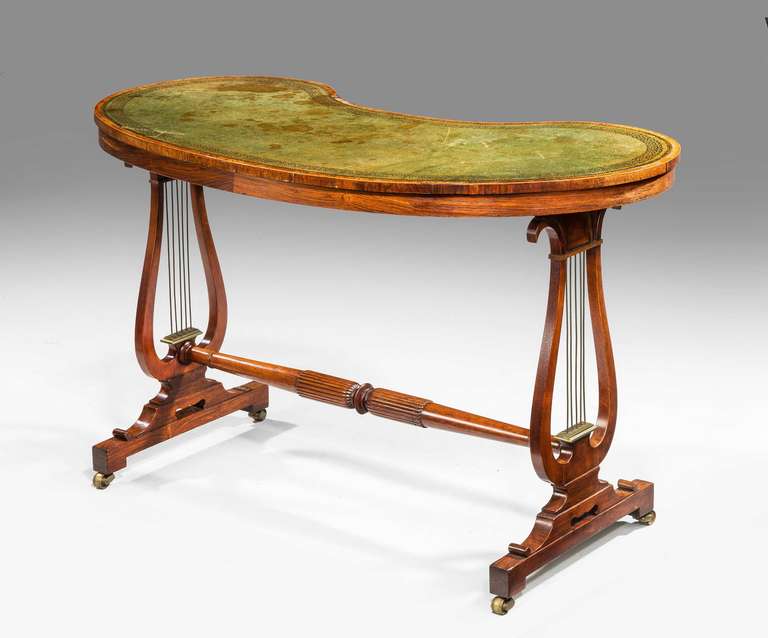 An elegant George III period faded rosewood kidney shaped writing table of the finest quality, the lyre end supports with gilt bronze rods with a double cross banded top and well turned stretcher on block scroll supports.

