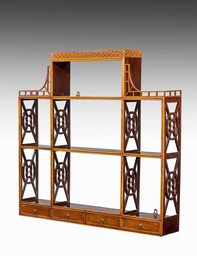 An exceptionally attractive set of hanging wall shelves, in two contrasting types of mahogany, with fretted geometric uprights and surmounted with a finely pierced top. The base incorporating four slender drawers.

RR.