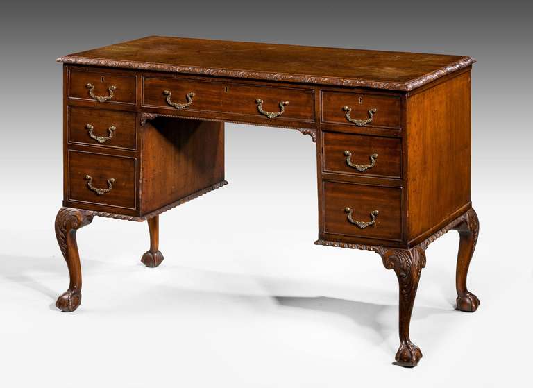An early 20th Century mahogany writing table of Chippendale design, the top boarder with continuous carved detail, well cast original brass handles, cabriole supports with acanthus over claw and ball feet.