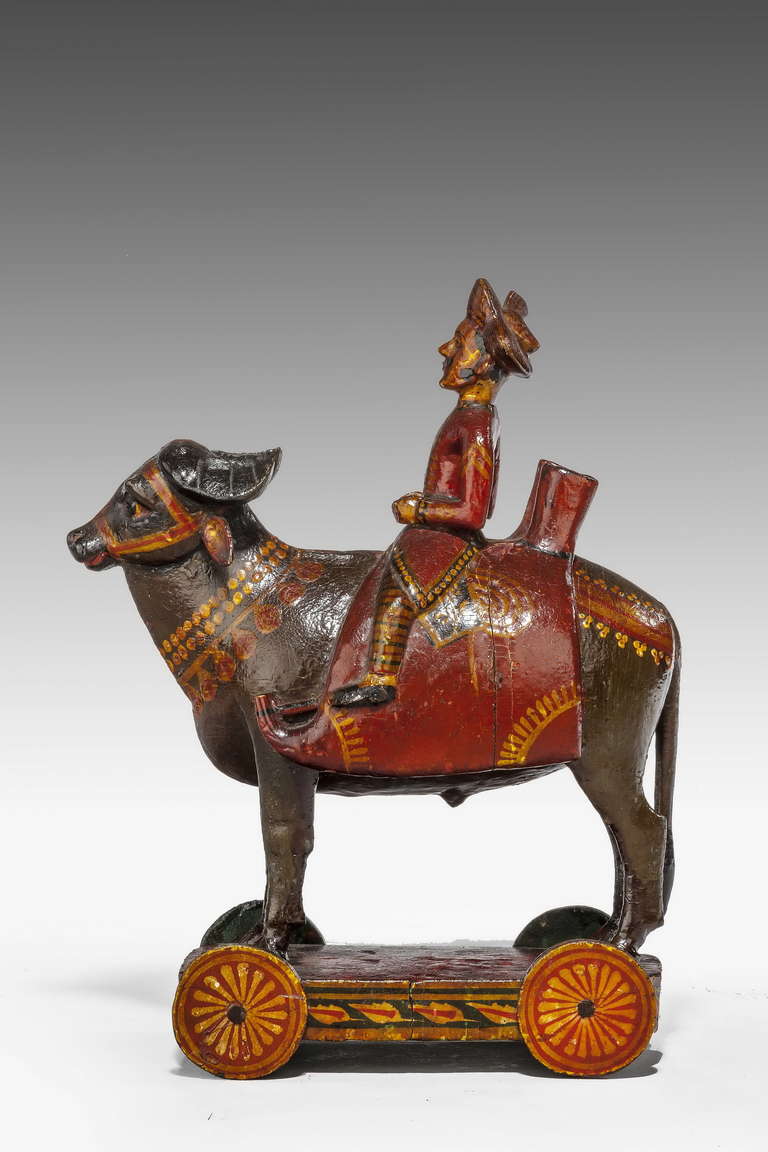 An early 20th century, amusing Indian polychrome figure astride an Oxen on a trolly base, original decoration.