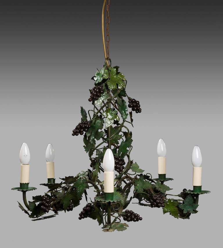 A green tole five-arm chandelier with elaborate vine leaves and hanging clusters of grapes, largely original decoration.