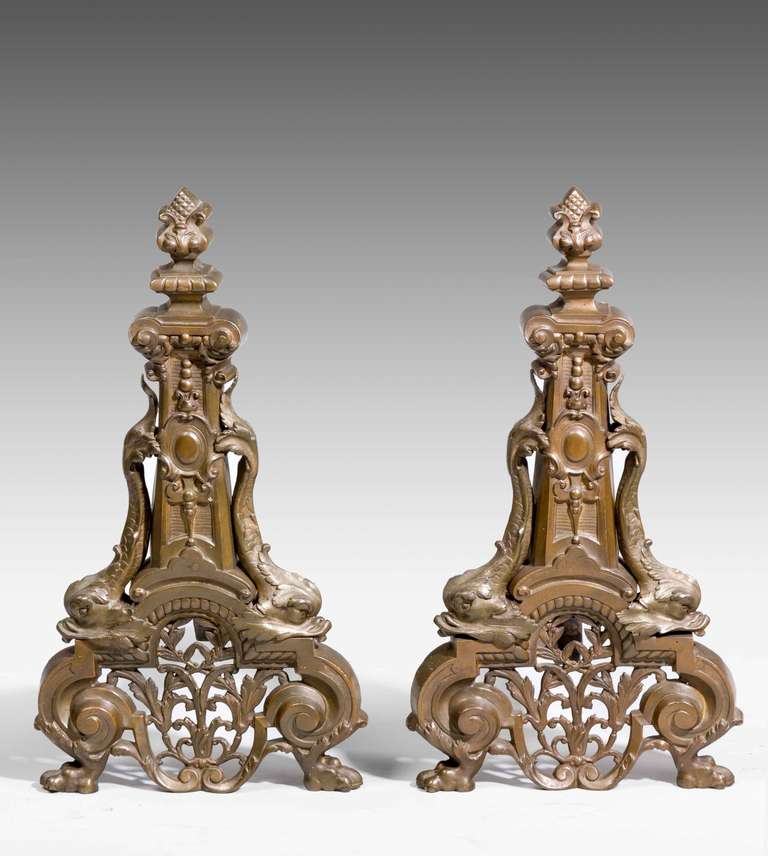 A large pair of cast iron andirons with good sculptured detail incorporating dolphins and scroll-work, bronzed finish.