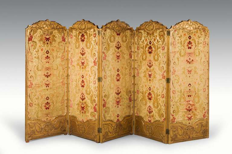A fine French giltwood four-fold screen, the top and base panels with exceptionally well carved detail with repousse decoration, the silk fabric now distressed.

