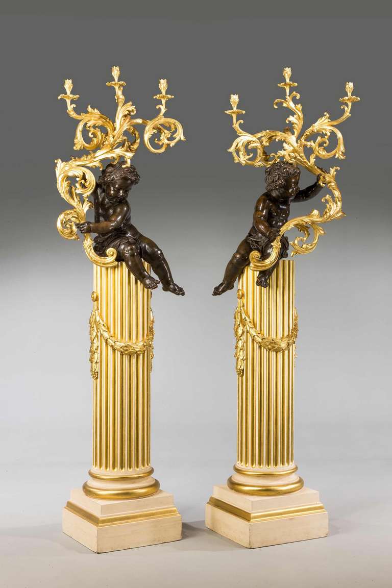 An outstanding pair of 19th century cold cast gilt bronze putti holding elaborate giltwood and gesso candelabra. The putti seated on well carved column bases, the bases decorated with suspended giltwood wreaths, circa 1890.
 
These highly