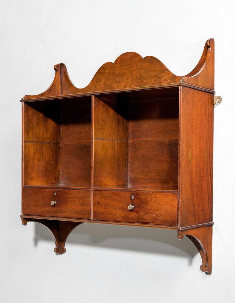 A George III period pale mahogany hanging shelves incorporating two-drawers to the base and originally with a central shelves.