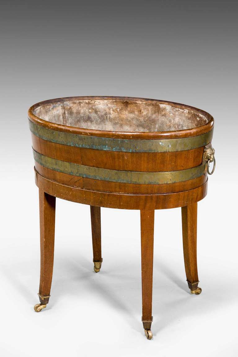 A late George III period mahogany wine cooler, the two broad and original brass bands over four square tapering supports, well cast and original handles.