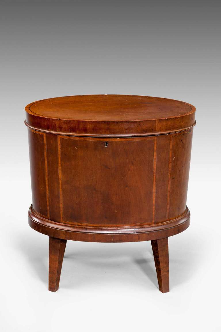A late George III period mahogany well-formed enclosed wine cooler, the top with banding and crossbanding on the surfaces of the edge, fine boxwood stringing on square tapering supports, the interior fitted with a single liner not original to the
