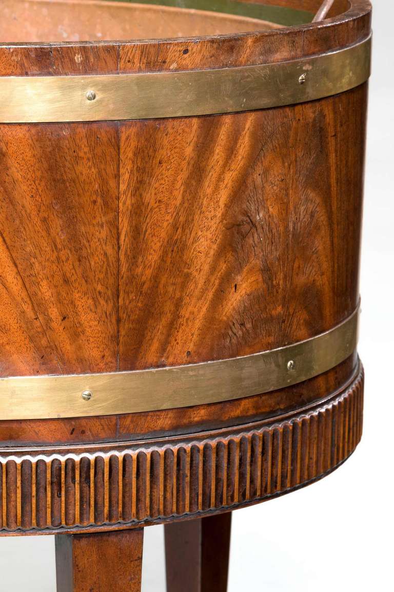 A well figured mahogany wine cooler/jardinière with an arcaded carved support with brass banding on square tapered supports terminating on spade feet.

RR.