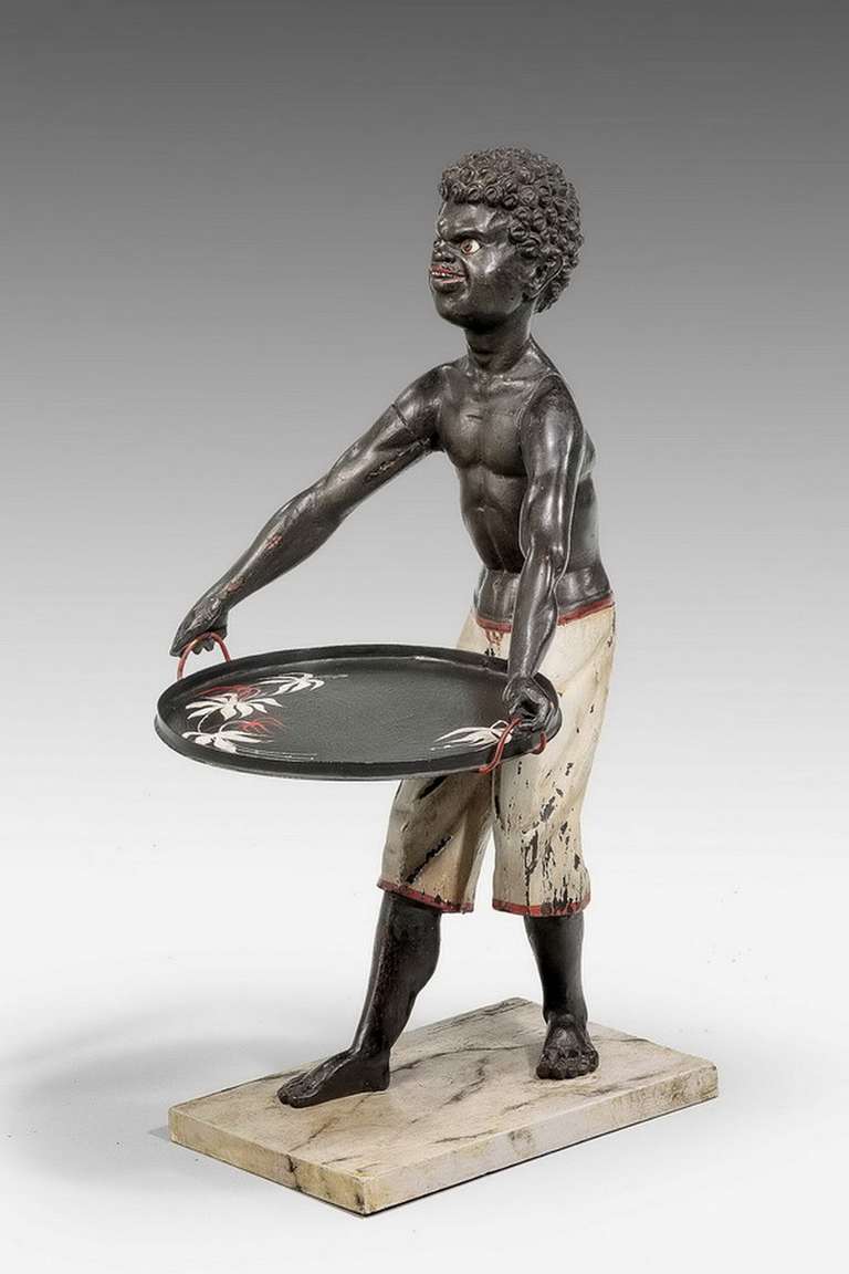 An amusing 19th century Toleware and carved wood card tray carrier retaining original decoration, the painting to the tray refreshed, the figure with glass eyes.

Provenance:
In the collectibles and antique industry, Toleware refers to