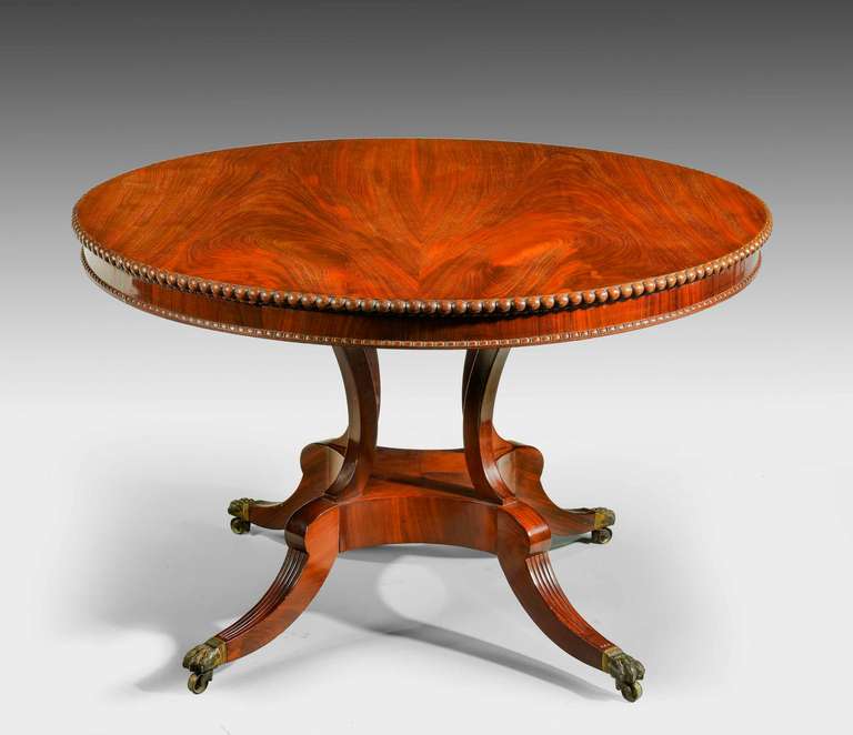 An exceptionally finely figured mahogany circular table of the regency period. The top with a substantial bead edge. On flared supports typical of Gillow’s, swept feet terminating in original shoes and castors. With beautiful and original brass