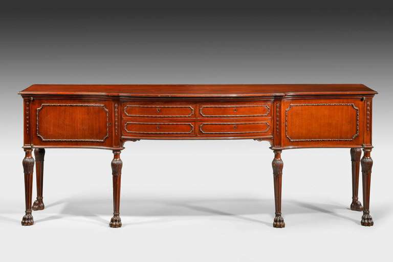 An elegant and unusually slender serpentine mahogany sideboard on elaborate tuned and fluted legs ending in hairy paw feet. The draw and cupboard fronts with a gently carved border.