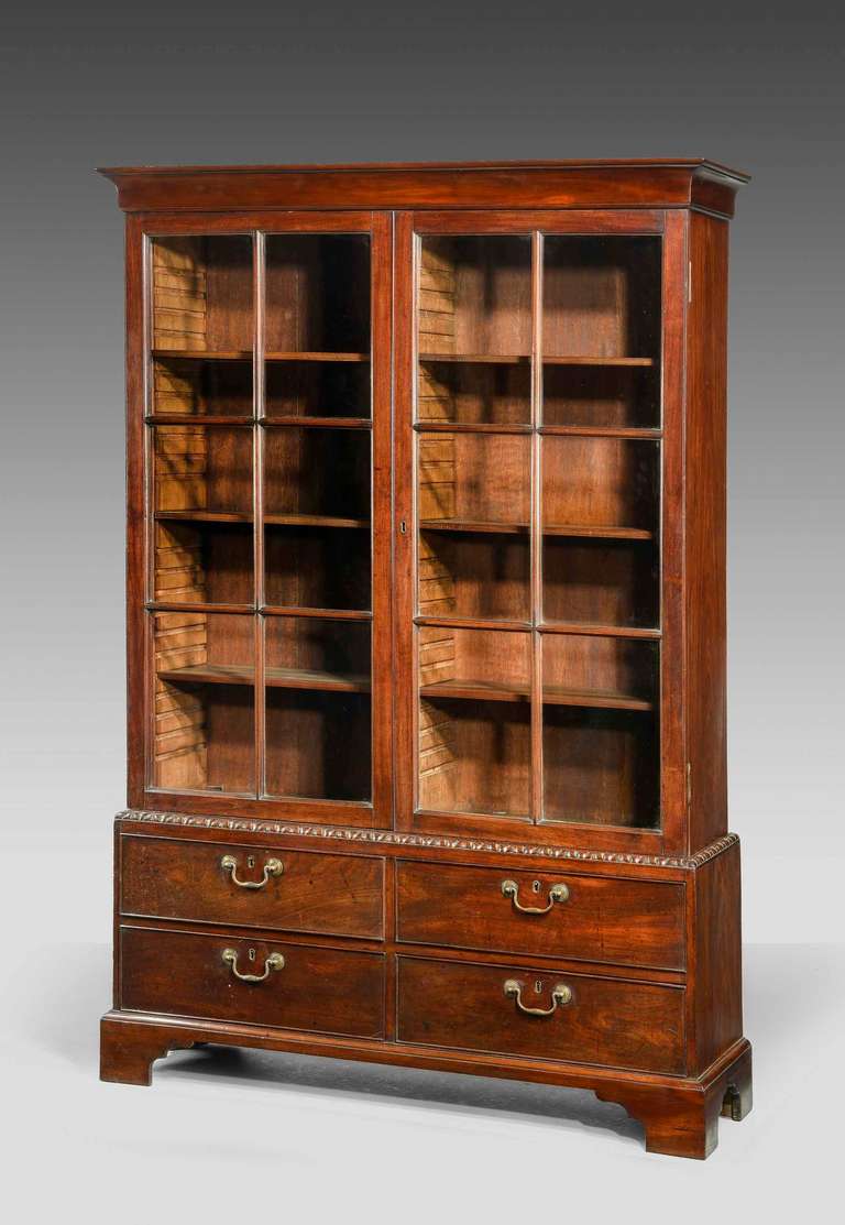 A good George II period mahogany Bookcase, low waisted with finely carved waist section. Plain six panel astragal glazed doors, the base containing four drawers.

Provenance
Curtiss and Sons Portsmouth Depository Label
