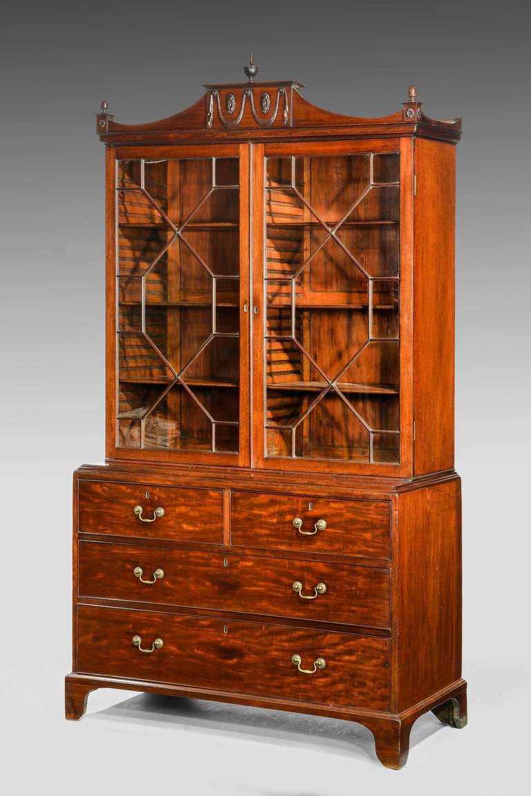 An elegant George III period mahogany bookcase on chest, the original pediment finely carved with neoclassical design details, astragal glazed doors, low waisted on bracket feet, the top and bottom associated.