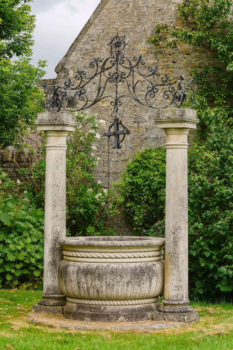 A finely carved stone well head, the two pillars along a massive circular bowl. The top with elaborate cast iron bucket supports section, late 20th century. Natural patina.