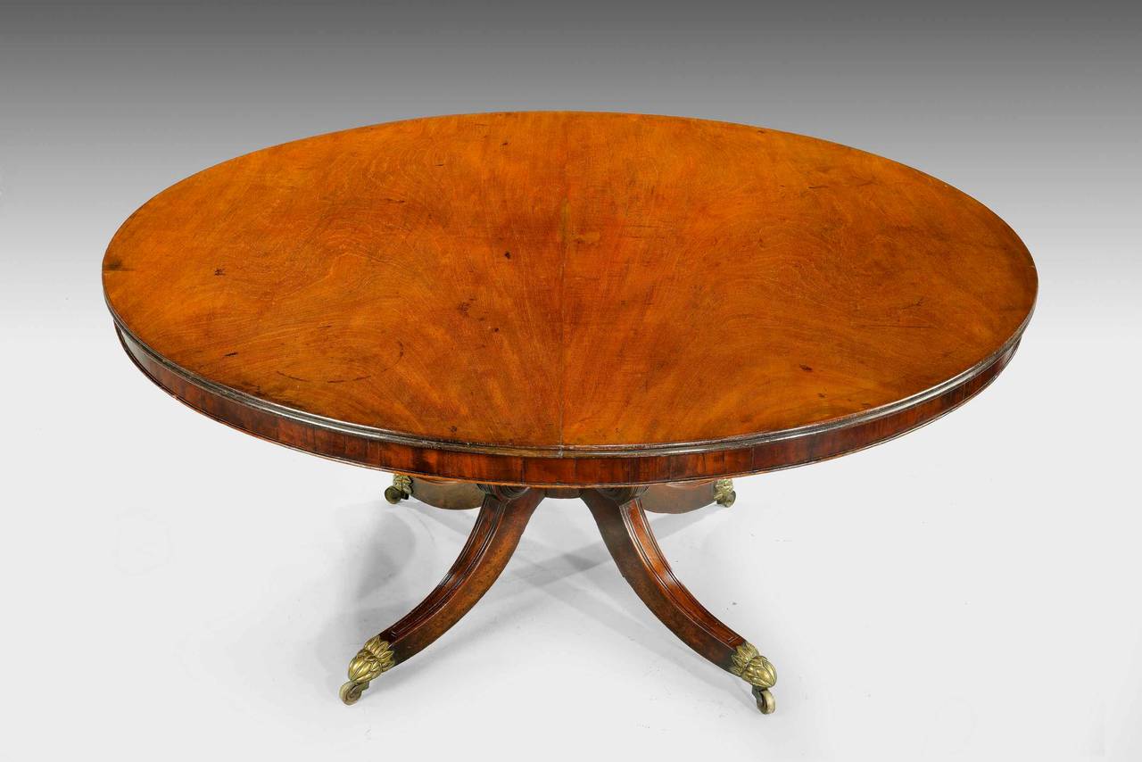 A very good Regency period mahogany circular table, the top with a slender border on a well turned central support with finely carved scroll swept feet, retaining very fine and original shoes and castors.