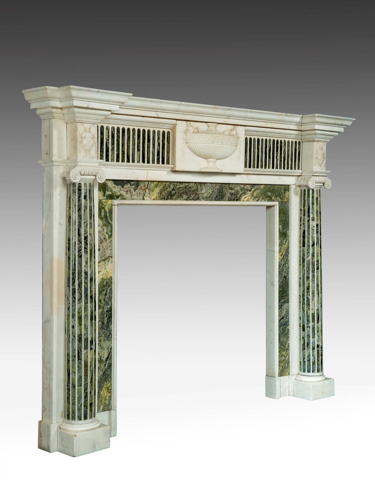 An important early 19th century marble fireplace. The jambs with elaborately inlaid pillars of contrasting marble. The tablet of good form, with drapes emanating from a cerated top. The top of the up rights with neoclassic urns and with floating