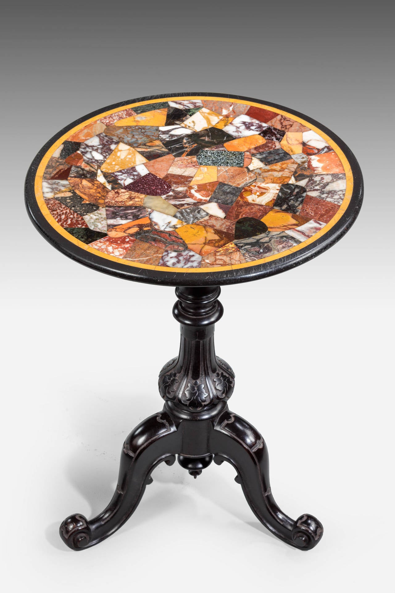 A well carved mid-19th century ebonized mahogany occasional table. The elaborately shaped and carved central stem over three cabriole supports terminating in French Scroll feet. The top beautifully inlaid with specimen marble and semi precious