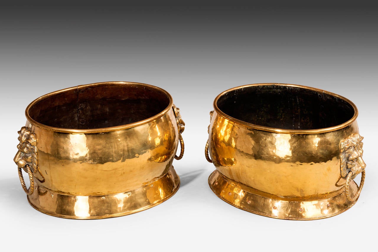 A good pair of oval heavy cast brass jardinières or wine coolers with massive lion handles supporting writhen rings.

