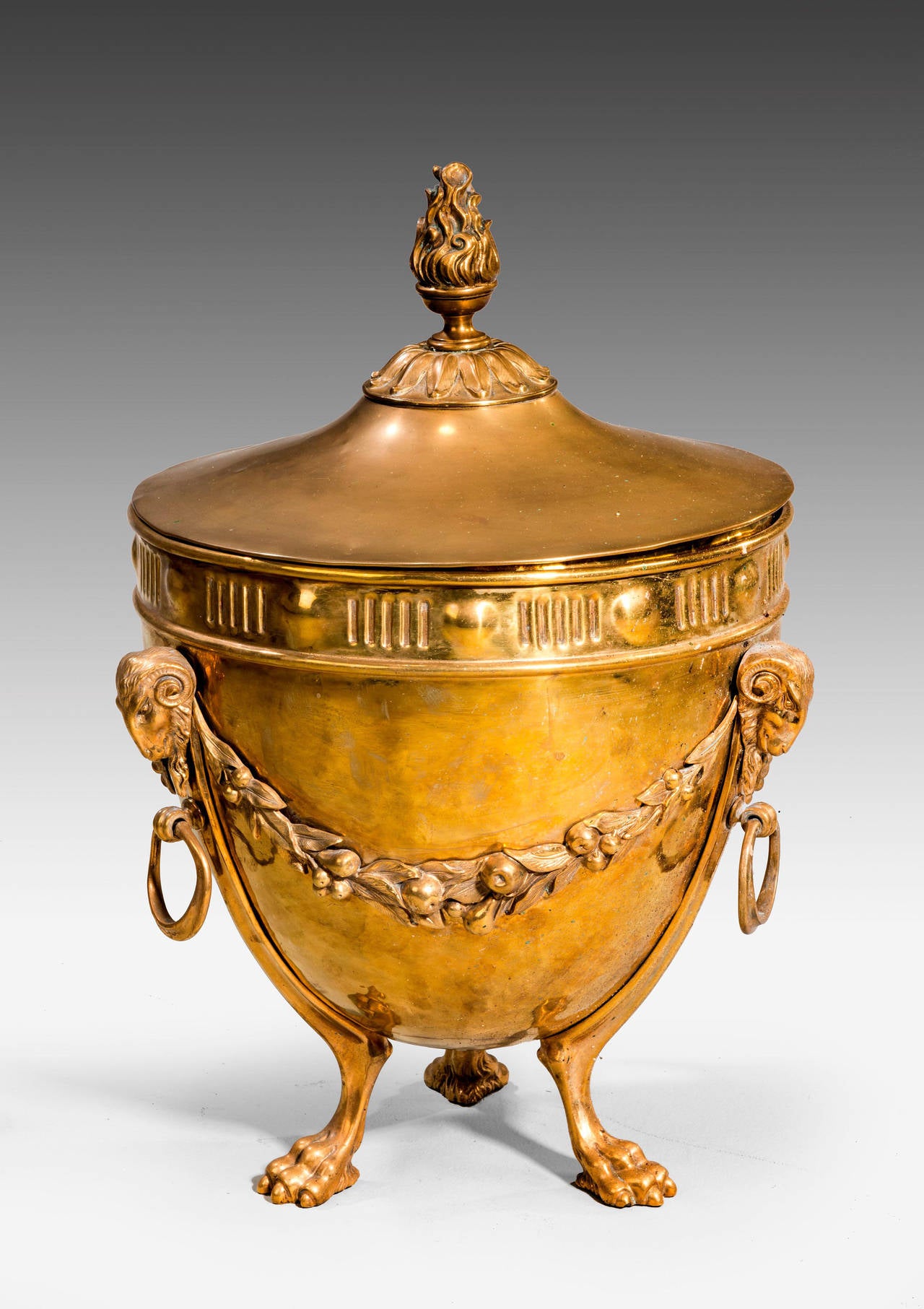 A circular 19th century coal container showing influences of Robert Adam. The main body with swags of plums and foliage. Rams heads to the top sections of the curved supports, ending in hairy paws. The top domed with flambé finials.