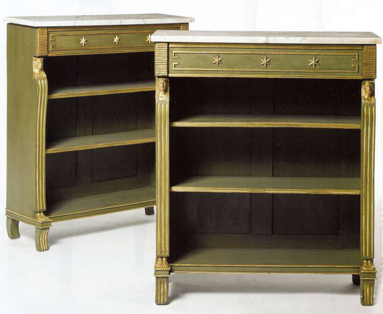 Green painted with gilt highlights and white marble tops, each case with two shelves, and a single drawer decorated with three gilt stars in relief, the sides with Egyptian motif pilasters commencing with a carved pharaoh head and terminating in
