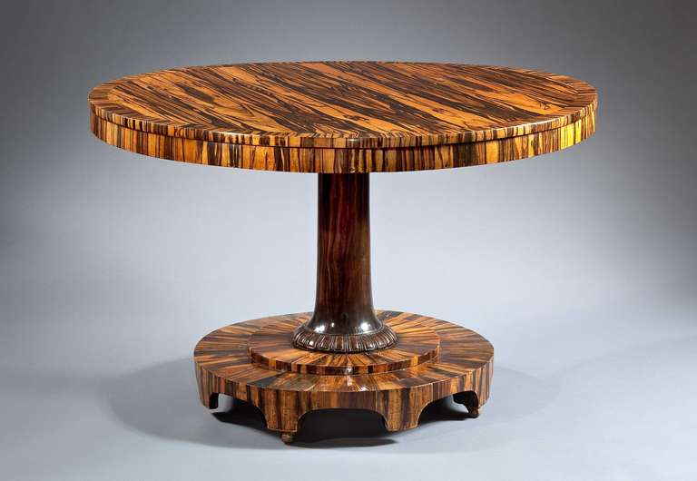 A highly figured drum table with rounded top and molded edge over frieze. Supported on center column standing on arched bracket base.  

Calamander ranks as one of the most desirable and expensive woods. Its drama comes from its bold figuration