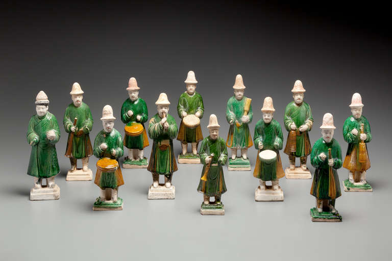 A Set of 12 Green Glazed Pottery Figures of Attendants and Musicians

Each figure standing on a small, green-glazed, graduated square base, dressed in a green-glazed robe that falls short of the unglazed boots, the head and high domed hats