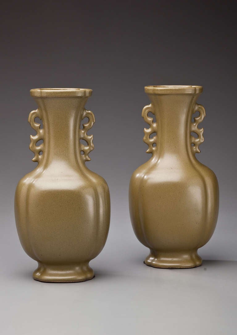 Each vase of quartelobed section, of lower, bulbous for rising from a splayed foot, the tall, flaring neck applied on either side with a scrollwork handle, all but the foot rim covered in the olive-green-tone glaze.