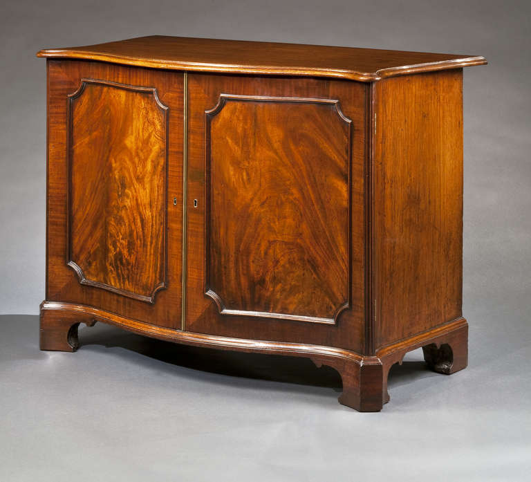 The shaped and molded rectangular mahogany top surmounts a pair of paneled doors which open to reveal four slides lined with red, blue, green and brown marbled paper, the whole raised on shaped bracket feet.