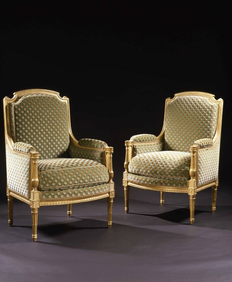 Each bergere fashioned with an arched seat back with channeled and striated decoration on top and beaded decoration on the front edges.  The lateral uprights surmounted with a foliate finial from which emanates the down-swept arm culminating in