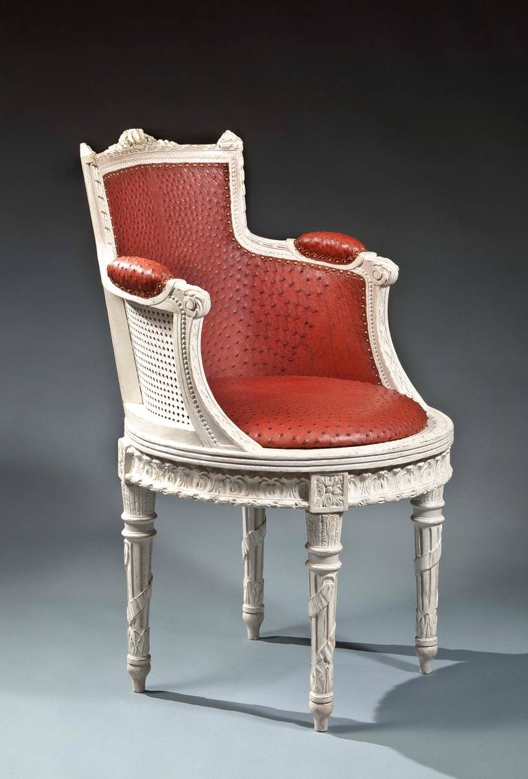 The molded backrest tapers to the curve of the rounded seat surmounted by a carved, stylized central medallion that extends into a continuous carved ribbon pattern through down swept armrests with red ostrich leather manchettes ending in scroll
