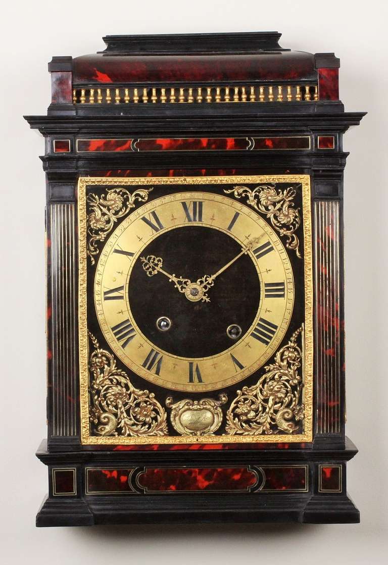 22-cm velvet covered dial, applied engraved brass chapter ring with Roman numerals and ful minute marking, foliate pierced and engraved brass hands, pierced cast brass spandrels with scrolls, flowers and dolphins flanking the hinged signature plate