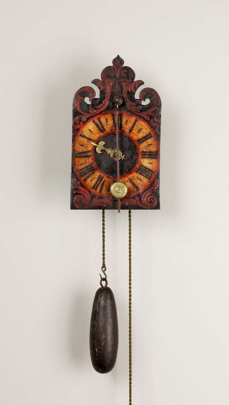 11-cm polychrome painted shaped dial with Roman numerals, single brass hour hand, weight driven movement with verge escapement and front pendulum of day duration, iron side doors, wall hoop and spurs.