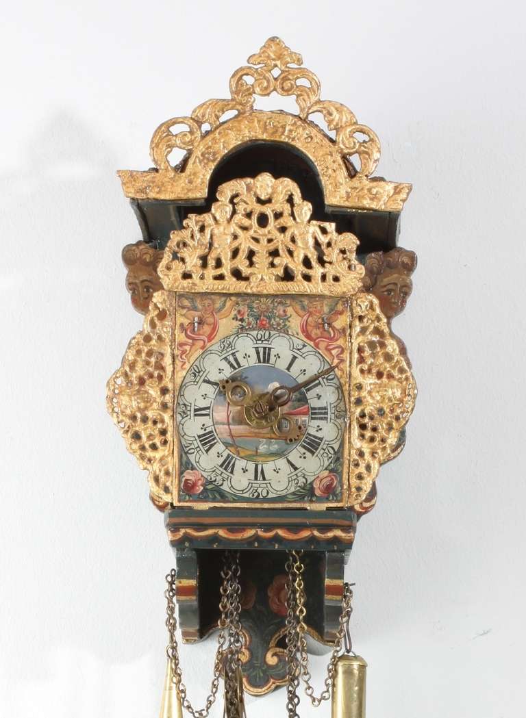 9-cm. polychrome painted dial with Roman numerals and five-minute arches, pierced brass hands and alarm disc, roses in the lower corners and deities flanking a basket on a gilt ground above, centre with landscape, brass weight driven pillar movement