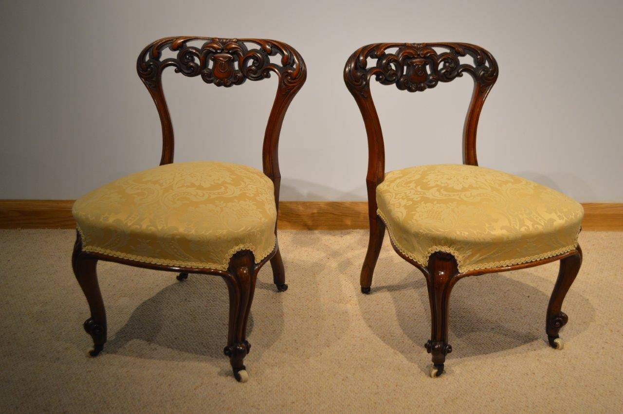A beautiful pair of small walnut Victorian Period nursing chairs. Each with a beautifully carved and pierced top rail with a central armorial bearing monogram. With shaped uprights, sprung newly re-upholstered seats and supported on slender cabriole