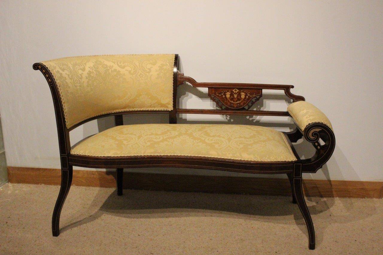 A mahogany inlaid Edwardian period antique settee. With a shaped curved and padded back having a mahogany pierced panel with marquetry and pen-work inlaid detail and a roll arm. The serpentine padded seat newly re-upholstered in a gold silk damask,