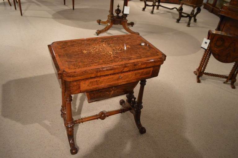 A Victorian period burr walnut inlaid games/sewing table. The rectangular top veneered in beautifully figured burr walnut with a central foliate marquetry inlaid panel cross banded in amboyna, which turns and opens to reveal a back gammon and chess