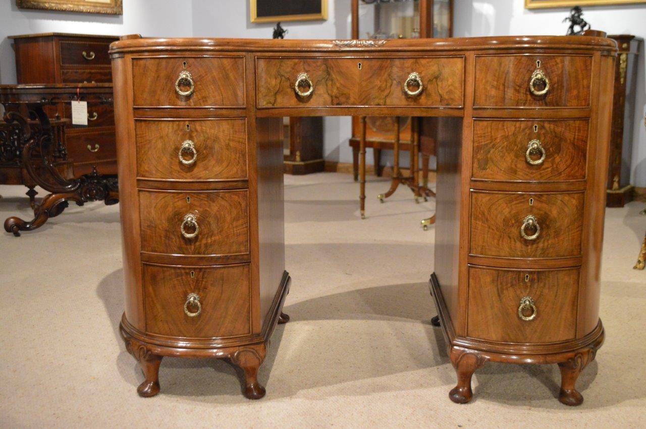 A walnut & burr walnut 1920s kidney shaped desk. The kidney shaped solid walnut top with a small raised walnut gallery and an inset olive green leather writing surface with gilt and blind tooled detail. Having nine mahogany lined drawers veneered in