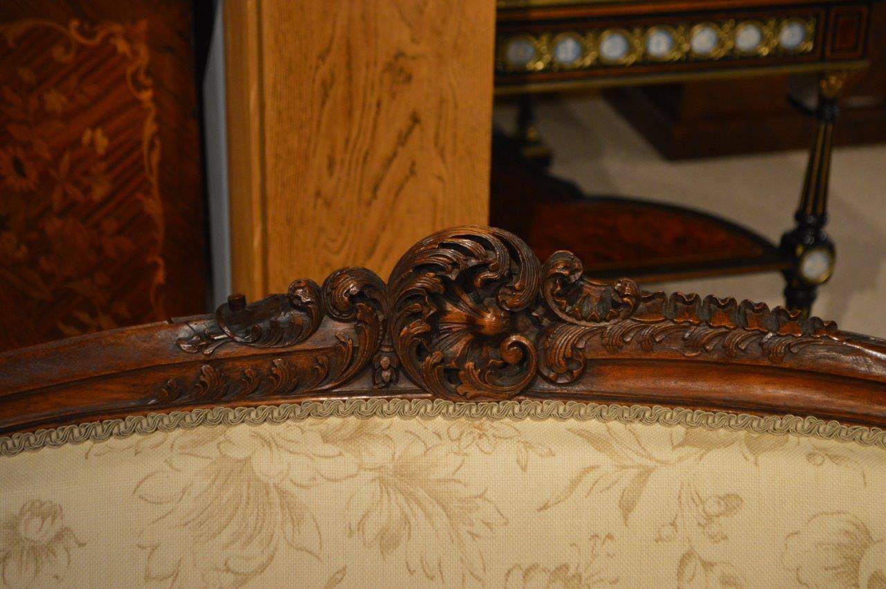 A  French Finely carved walnut antique settee/canapé. With a finely carved shell cartouche and further fine floral carved detail to the back and arms. Having three shaped padded back rests and a generous sprung seat newly re-upholstered in a beige
