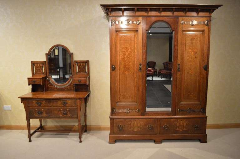 An Oak Arts & Crafts Period wardrobe & dressing table by Shapland & Petter of Barnstaple. The wardrobe having a deep overhanging moulded cornice above a central arched bevelled mirrored door, flanked by twin panelled doors each with wonderful copper